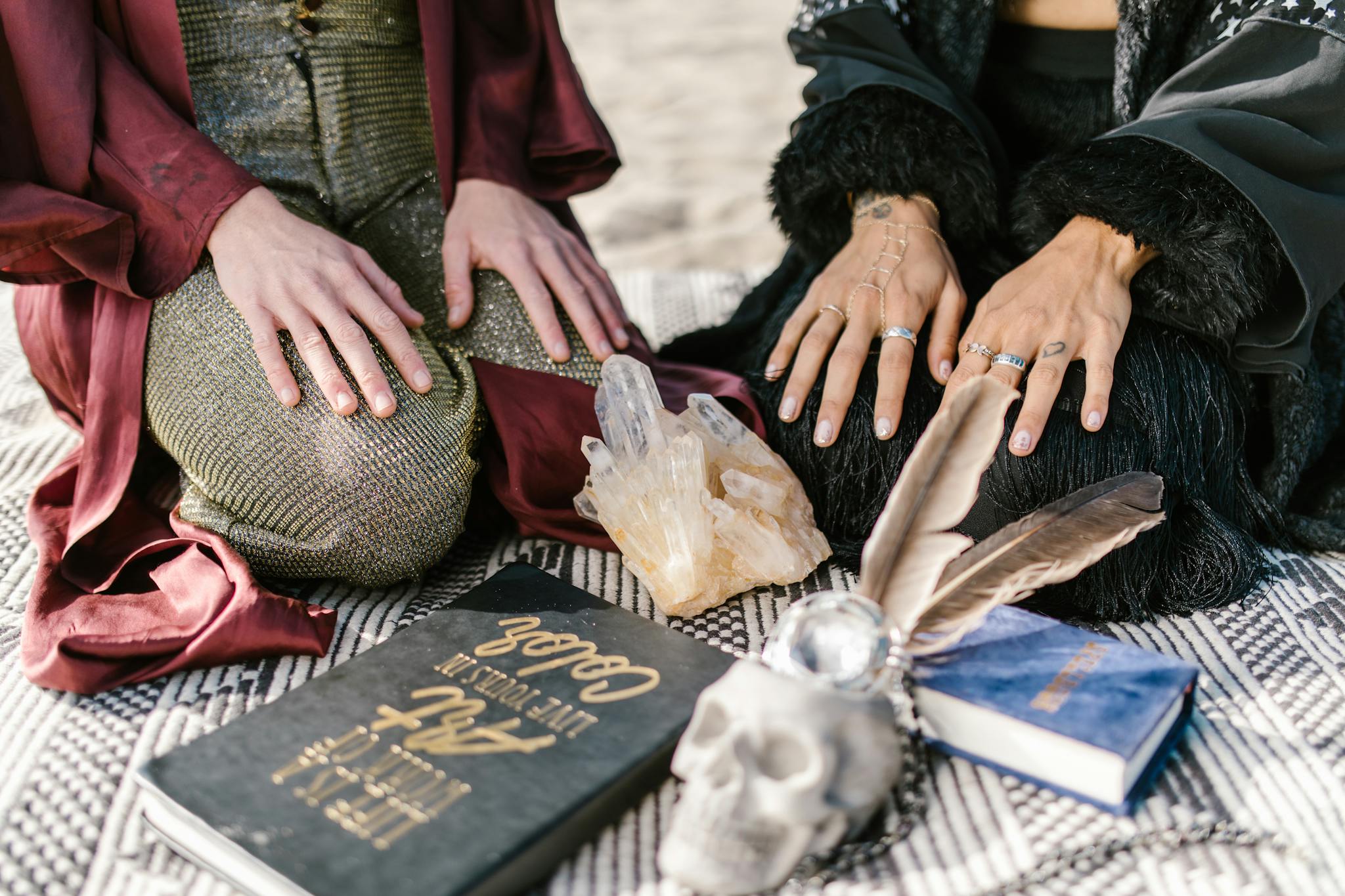 A mystical scene with crystals, a skull, books, and hands in contemplative poses.