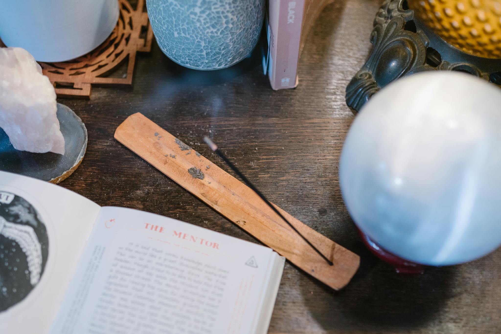 A mystical table setting with a crystal ball, open book, crystals, and incense.