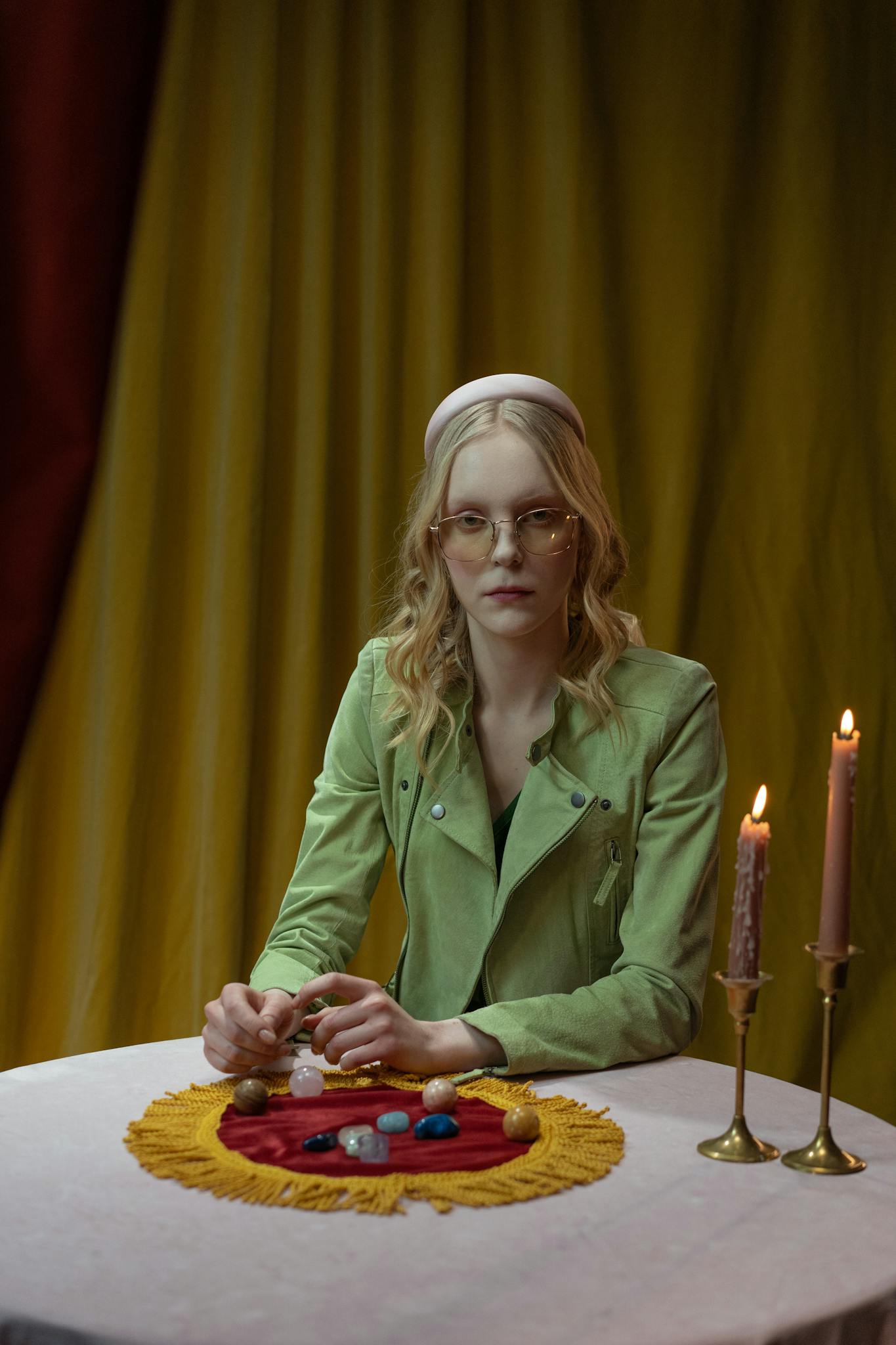 A woman sits at a table with candles and crystals, creating a mystical atmosphere.